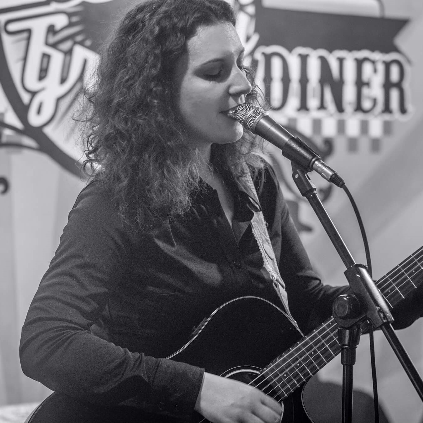 Nicole Stella playing an acoustic guitar and singing