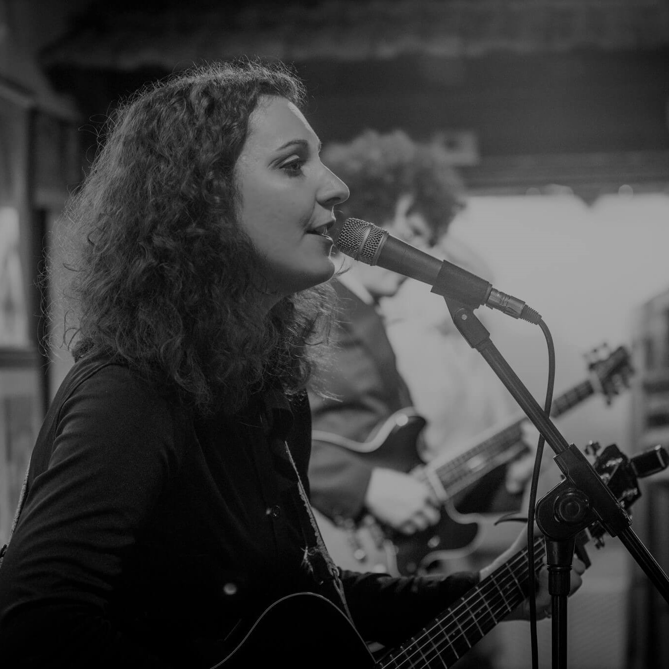 Nicole Stella singing and playing an acoustic guitar