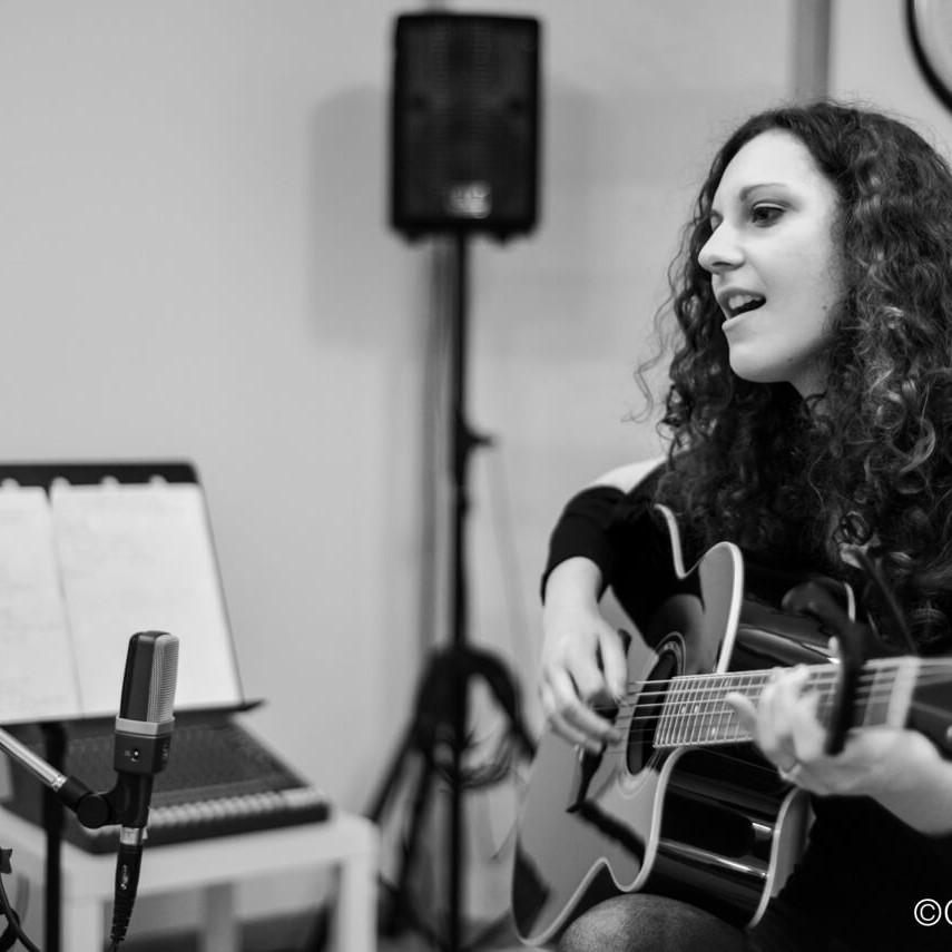 Nicole Stella singing and playing an acoustic guitar