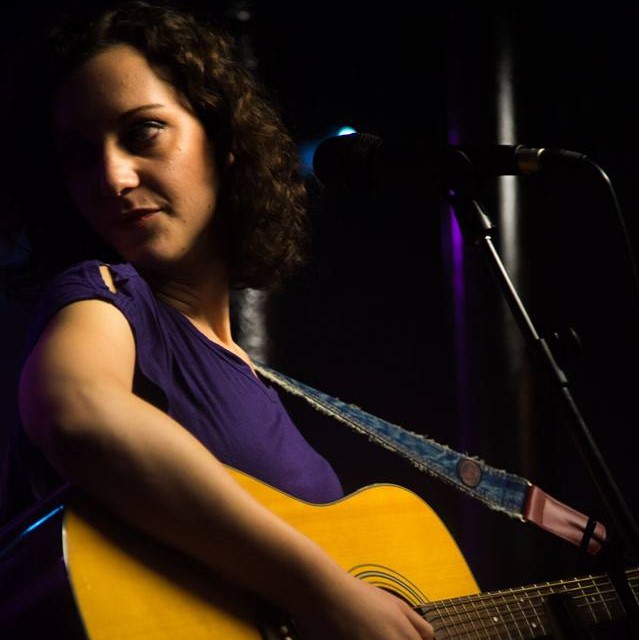 Nicole Stella singing and playing an acoustic guitar