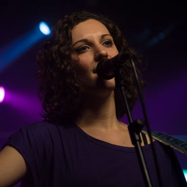 Nicole Stella singing and playing an acoustic guitar